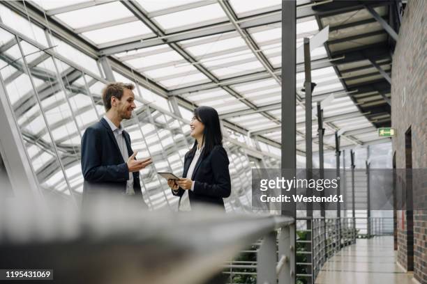 smiling businessman and businesswoman with tablet talking in modern office building - digital catwalk stock pictures, royalty-free photos & images