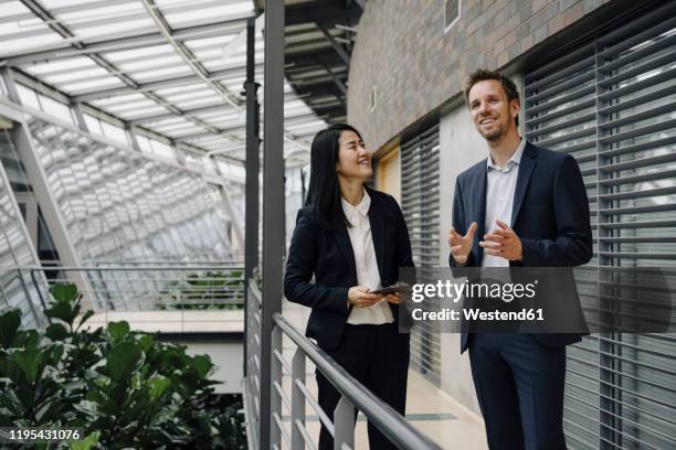 businessman and businesswoman with tablet talking in modern office building - metal catwalk stock pictures, royalty-free photos & images