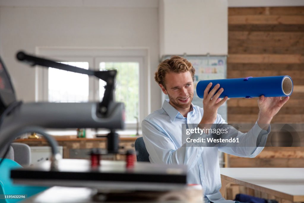 Young businessman in his office, looking through blue pipe