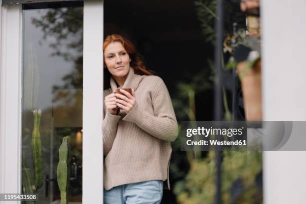 woman leaning in door, drinking coffee - woman day dreaming stockfoto's en -beelden