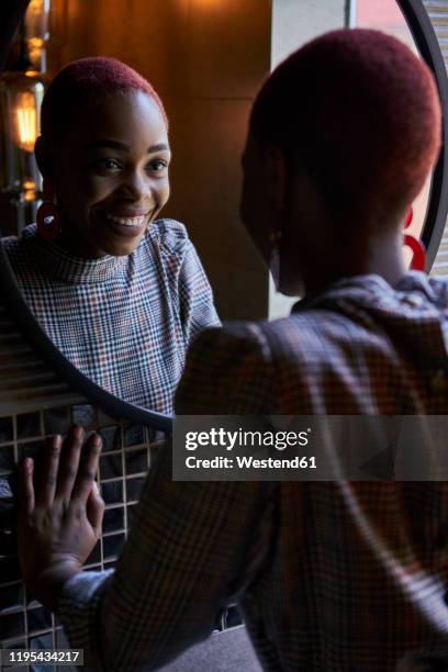 young woman with short haircut looking and smiling to her reflection in a round mirror - vestido a cuadros fotografías e imágenes de stock