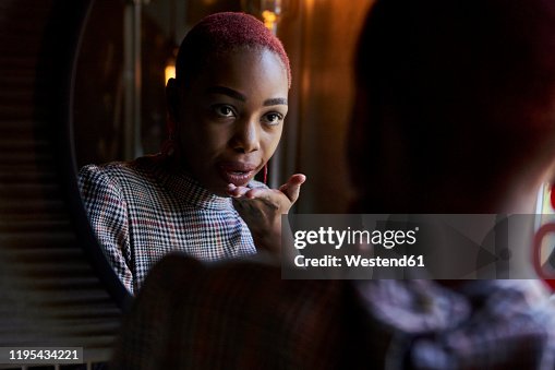Young woman with short haircut looking to her reflection and sending a kiss in a mirror Young woman with short haircut looking to her reflection and sending a kiss in a mirror