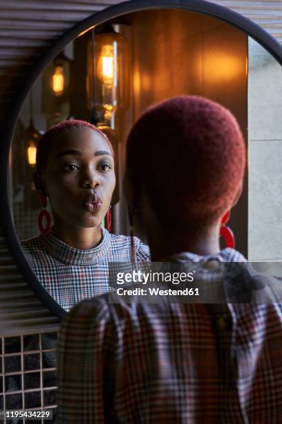 young woman with short haircut looking to her reflection and sending a kiss in a round mirror - short hair photos et images de collection
