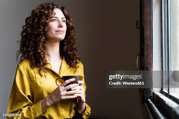 woman looking out of window with coffee cup - yellow blouse foto e immagini stock