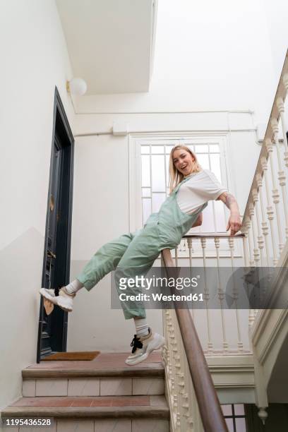 carefree young woman sliding on railing in staircase - sliding stock-fotos und bilder