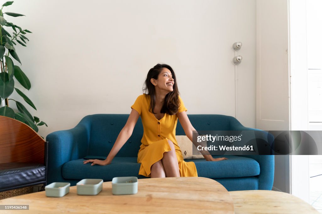 Happy young woman sitting on couch looking sideways