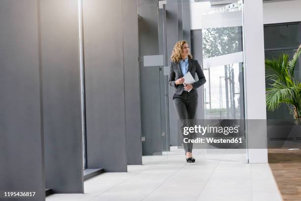 confident businesswoman holding tablet walking in office - pant suit stockfoto's en -beelden