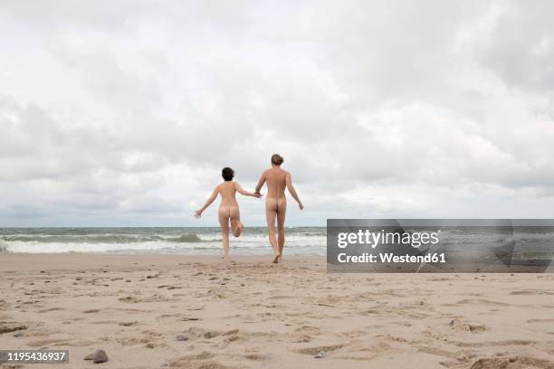 nude couple running to the sea, holding hands - nudity foto e immagini stock