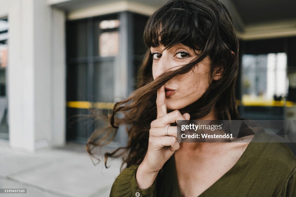 Portrait of smiling brunette woman, finger on mouth