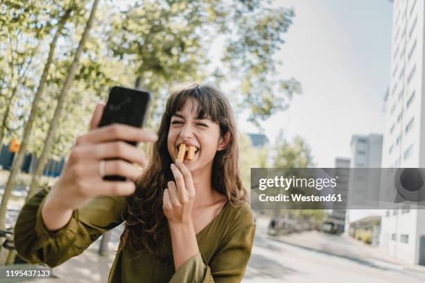 portrait of brunette woman, taking a selfie, rabbit teeth with french fries - brunette smiling stock-fotos und bilder