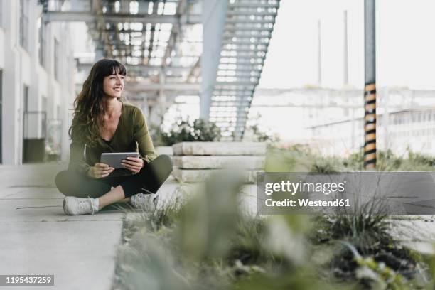 young smiling woman sitting on the ground and using tablet - benelux stockfoto's en -beelden