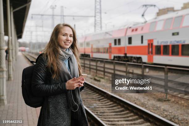 smiling woman waiting on platform using smartphone and earphones, vilnius, lithuania - lithuania woman stock pictures, royalty-free photos & images