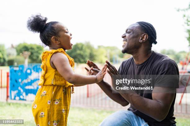 happy father and daughter playing a clapping game in a park - african hands clap stock-fotos und bilder