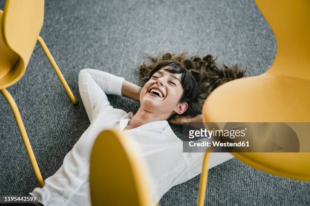 laughing businesswoman laying in an office on the floor between chairs - happiness stock-fotos und bilder