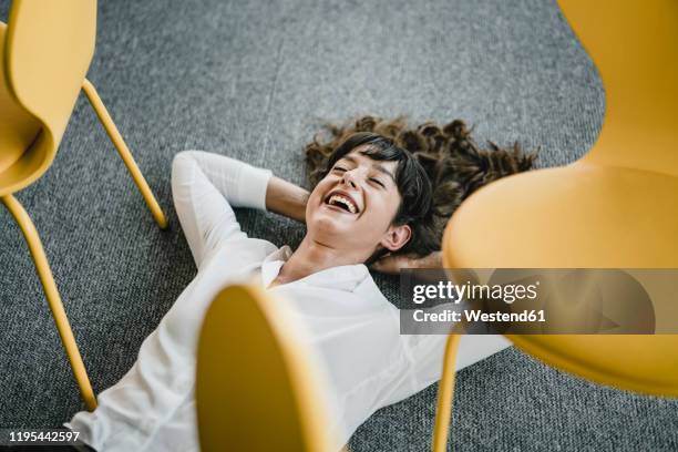 laughing businesswoman laying in an office on the floor between chairs - besetzt oder frei stock-fotos und bilder