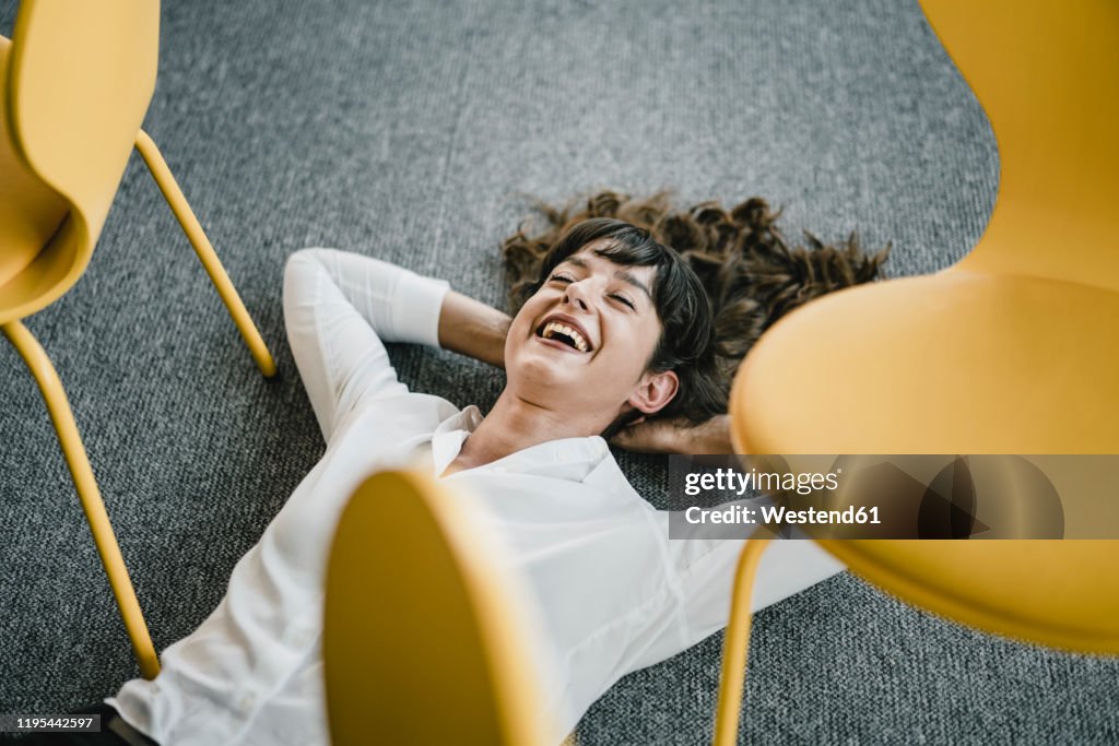 Laughing businesswoman laying in an office on the floor between chairs