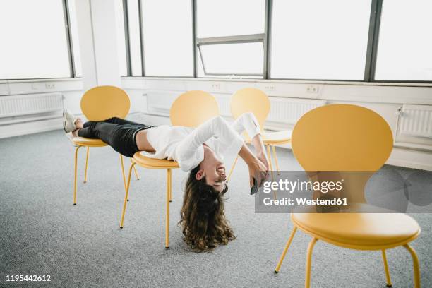 smiling businesswoman lying across chairs in an empty office using smartphone - gründer stock-fotos und bilder