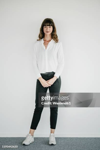 smiling businesswoman standing in front of a white wall - full body stockfoto's en -beelden