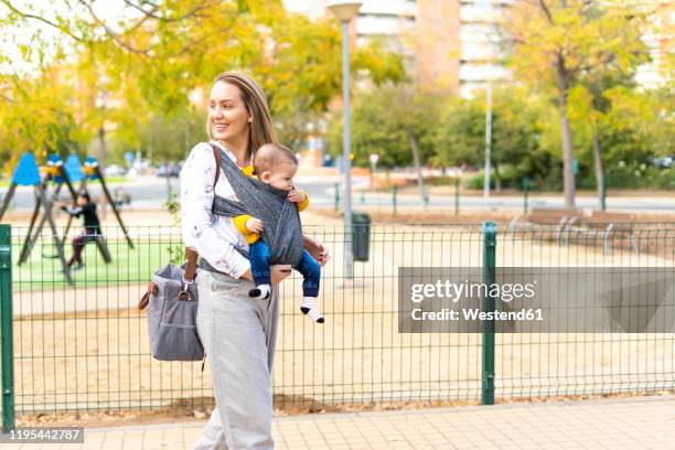 happy mother walking with baby boy in sling outdoors - baby bag bildbanksfoton och bilder