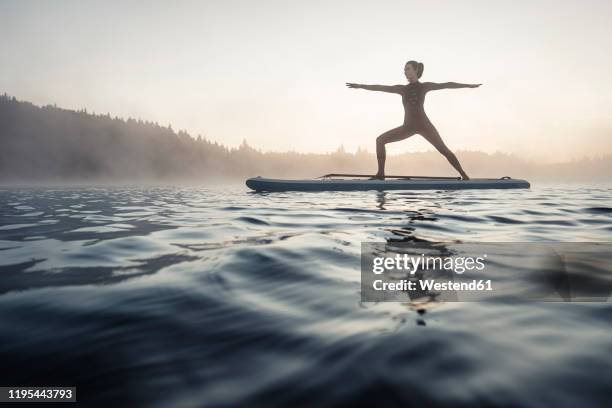 woman practicing paddle board yoga on lake kirchsee in the morning, bad toelz, bavaria, germany - practioners enjoy serenity of paddleboard yoga stockfoto's en -beelden