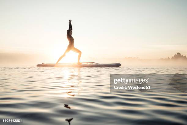 woman practicing paddle board yoga on lake kirchsee in the morning, bad toelz, bavaria, germany - water sports stock pictures, royalty-free photos & images