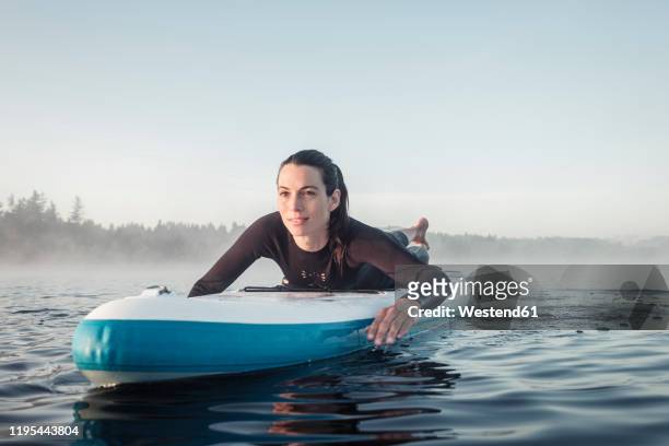woman lying on inflatable sup paddleboard on lake kirchsee, bad toelz, bavaria, germany - paddelbrett stock-fotos und bilder