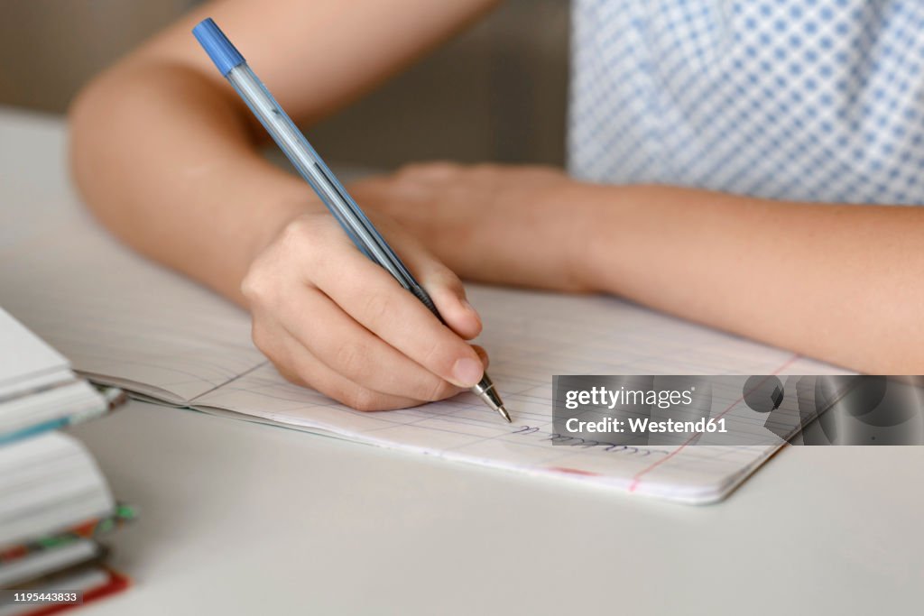 Close-up of girl sitting at table at home writing in workbook