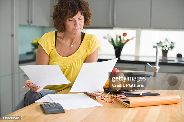 woman sitting in kitchen with bills - calculator stock pictures, royalty-free photos & images