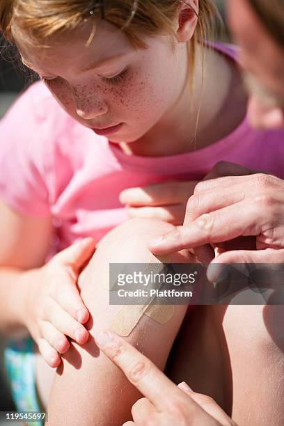 father sticking adhesive bandage on his daughters knee - wunder stock-fotos und bilder