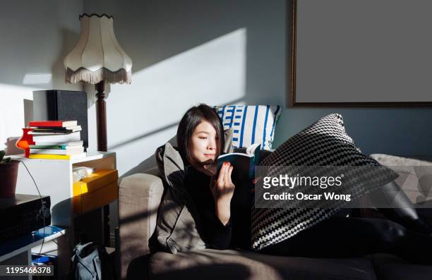 Young woman sitting on safe reading a book at home in a cosy atmosphere
