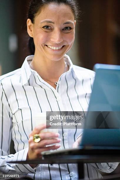 portrait of mature businesswoman with laptop, holding takeaway coffee - striped shirt stock pictures, royalty-free photos & images
