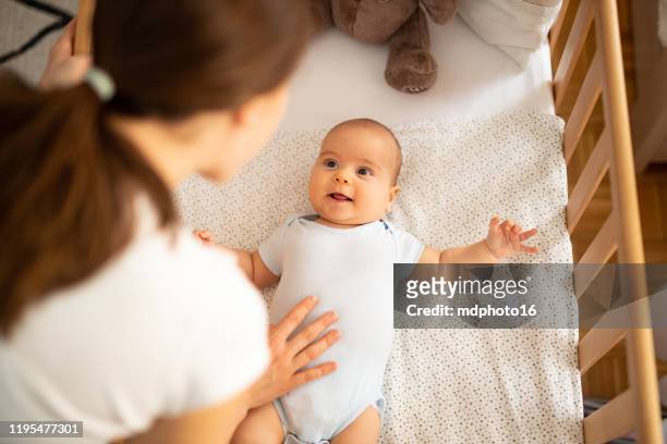 mamma che mette a dormire il suo bambino. donna che si china in avanti su un presepe per controllare il suo bambino. - culla foto e immagini stock