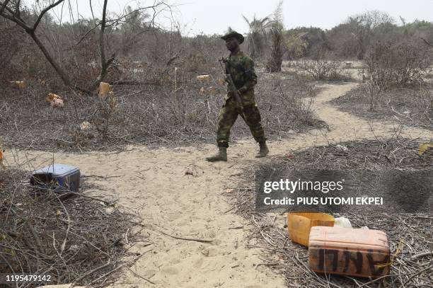 Naval personnel walk past jerrycans abandoned by vandals stealing from oil pipelines belonging to the Nigerian National Petroleum Company close to...