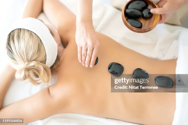 beautiful young woman undergoing treatment with hot stones in spa at hotel resort. - terapia lastone fotografías e imágenes de stock