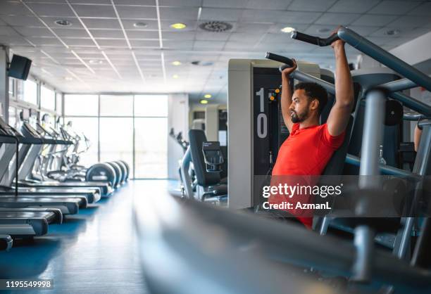 afrikanischer mann mit schulterpresse im fitnessstudio - schulterpresse stock-fotos und bilder
