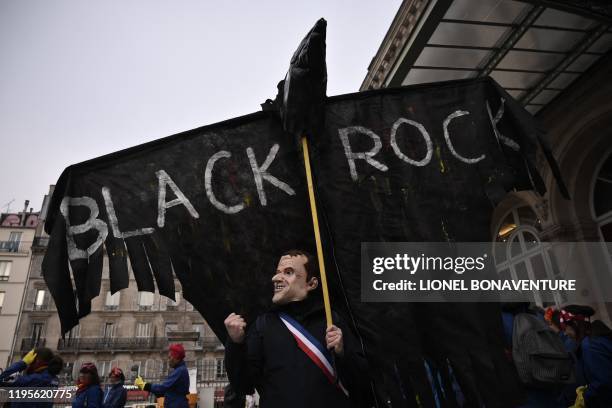 Man wearing a mask depicting French President Emmanuel Macron holds a puppet shaped as crow and reading BlackRock, as US global investment management...