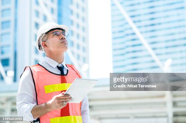 construction engineer wearing protective helmets and vests discussing project details at construction site. - business man overseeing blueprints outdoor stock-fotos und bilder