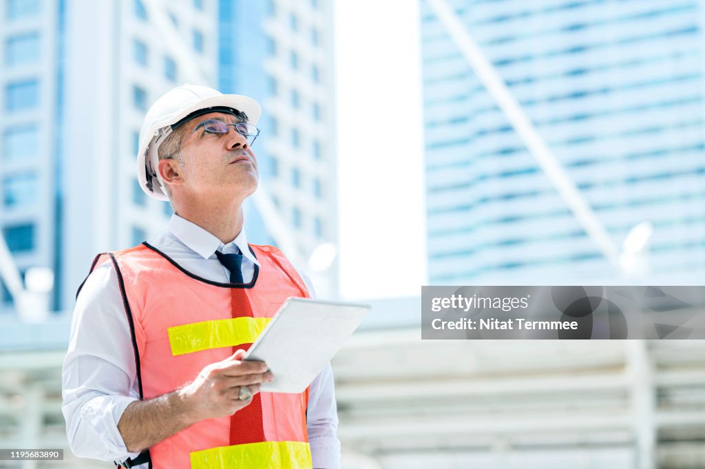 Construction engineer wearing protective helmets and vests discussing project details at construction site.