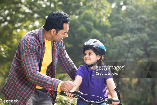 father teaching his son cycling at park - father helping son wearing helmet stock pictures, royalty-free photos & images