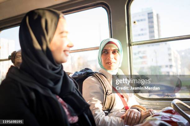 two middle eastern females riding in public transportation - kids sitting together in bus stock-fotos und bilder