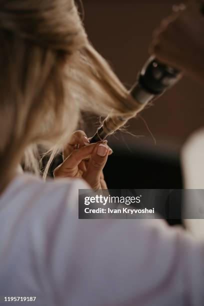 bride twists the hair with a curling iron at home. preparation of the bride. close up. women doing hairstyle herself and using straightener on beautiful long curl hair. beauty and haircare concept - love woman photos et images de collection