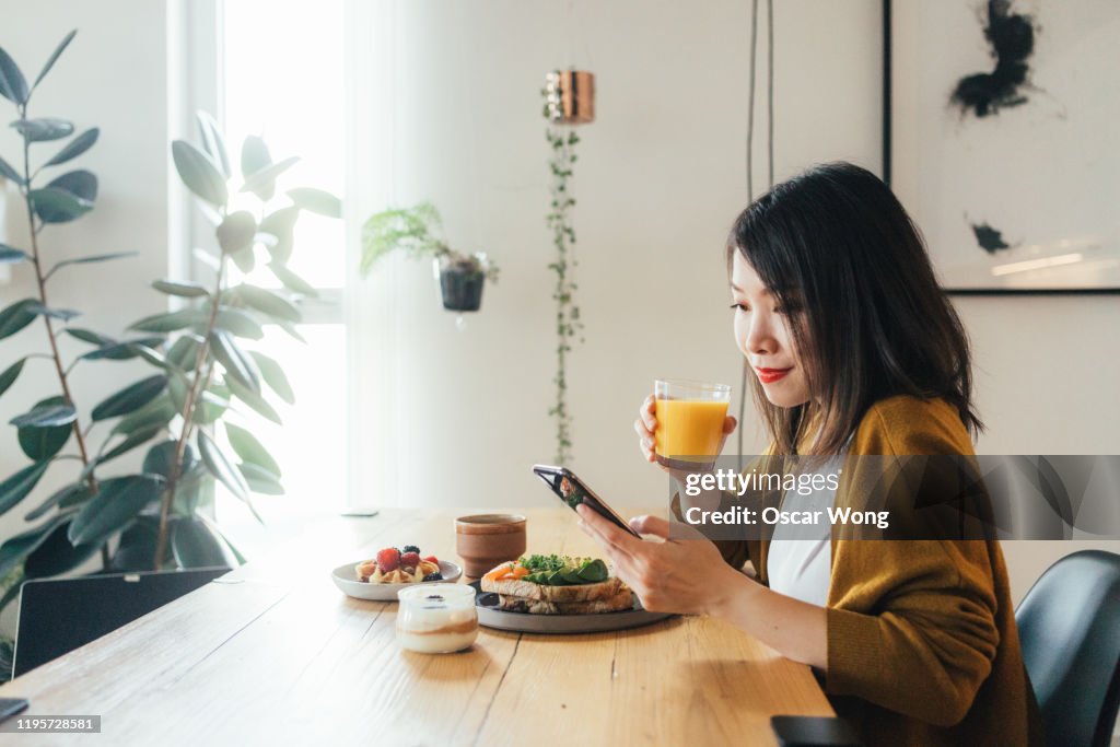 Young beautiful woman using phone while having breakfast