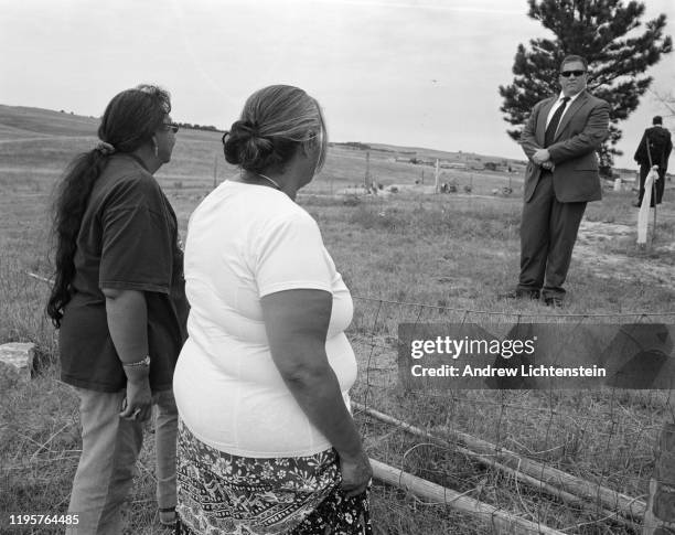 Two Lakota women from the Pine Ridge Reservation look on as secret service agents guard the perimeter of the Wounded Knee cemetery during a visit by...