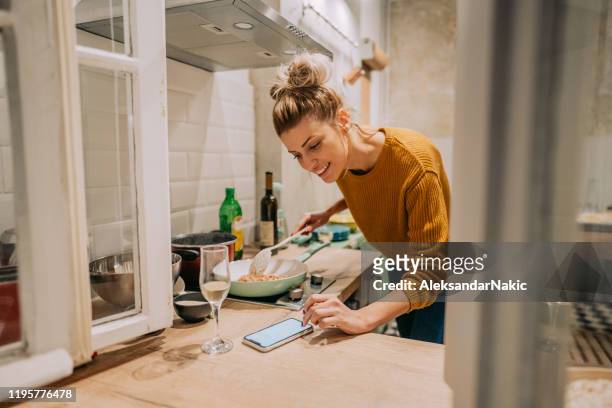 checking pasta recipe online - young woman cooking in kitchen stock pictures, royalty-free photos & images
