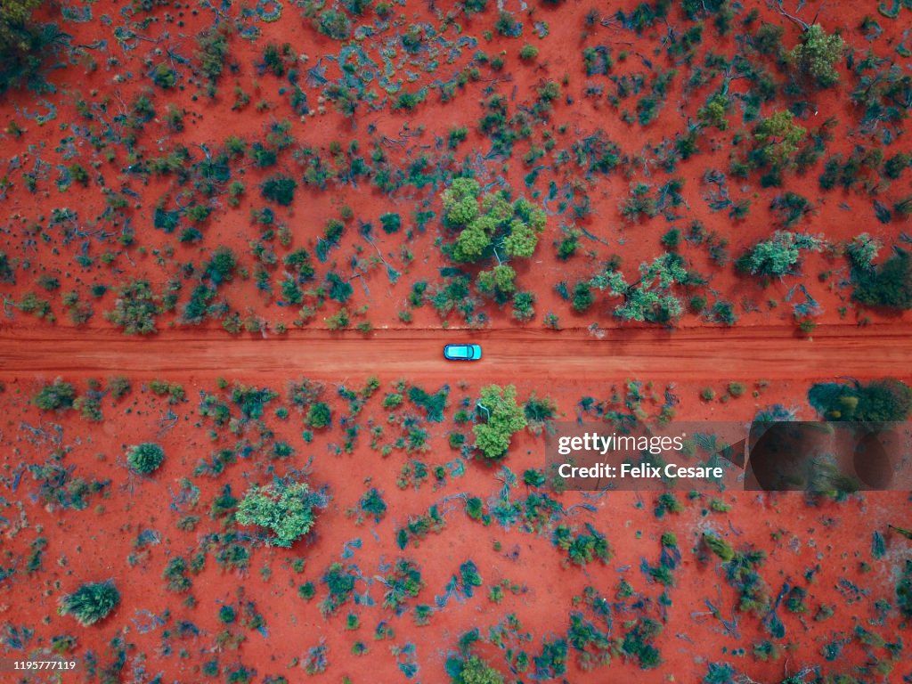 An Aerial shot of a car driving on the red centre roads in the Australian Outback