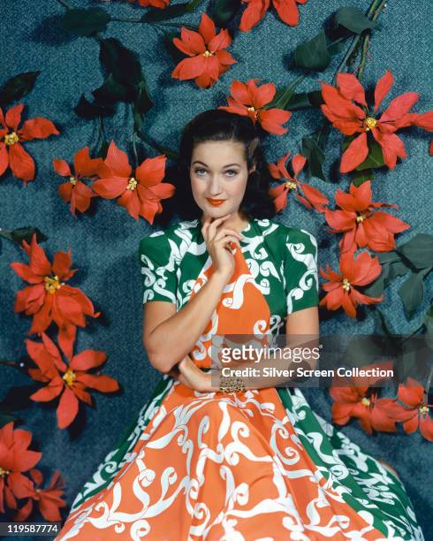 Dorothy Lamour , US actress, wearing a green and orange dress in a studio portrait, against a blue background with red flowers, 1940.