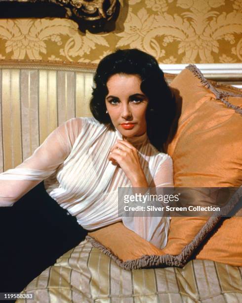 Elizabeth Taylor , British actress, wearing a sheer white blouse reclining against a cushion on a sofa in a studio portrait, circa 1955.