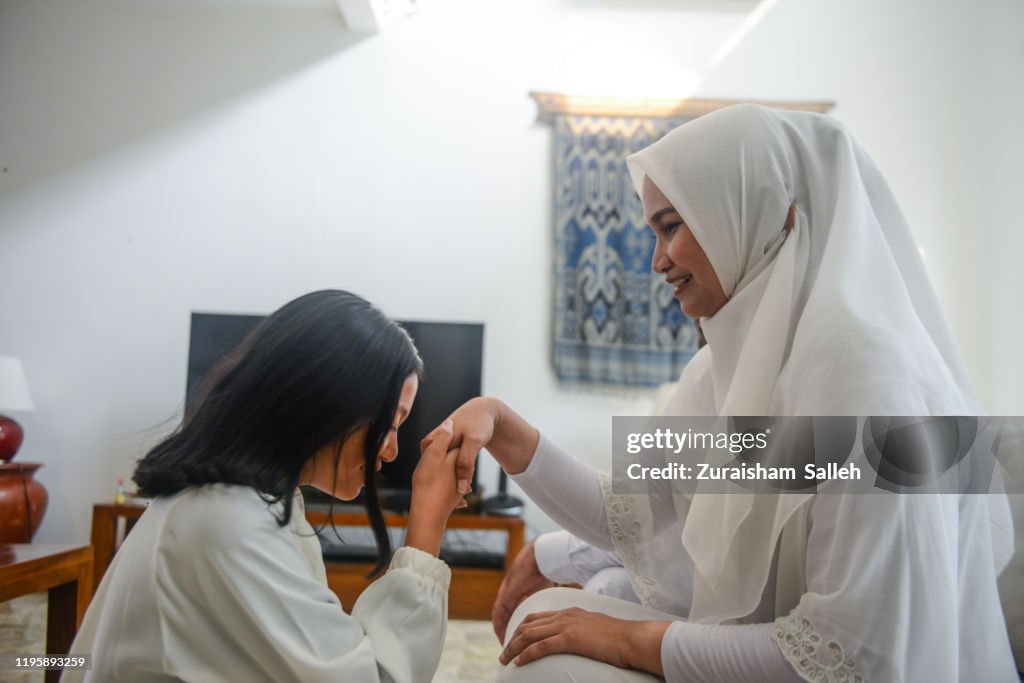 Asian Muslim girl kisses her mother’s hand during Hari Raya Puasa celebration