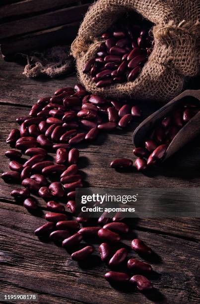 close-up low key image of red beans or kidney beans in burlap sack on rustic wooden table - red bean stock pictures, royalty-free photos & images