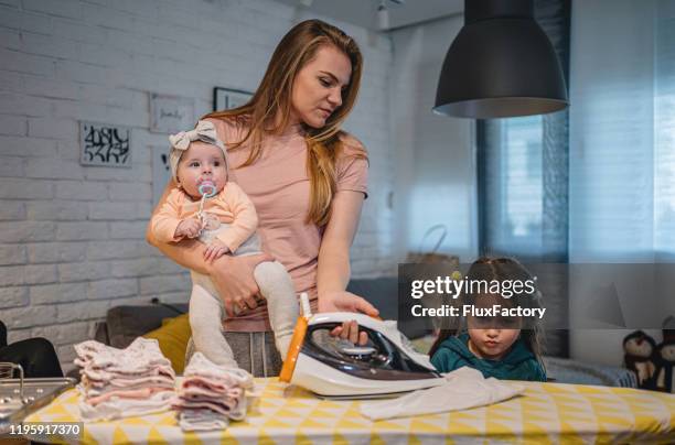 young mother ironing while caring for two daughters at home - stressed mother stock pictures, royalty-free photos & images